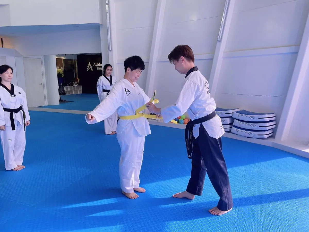 Adult taekwondo student receiving a yellow belt at a grading in Singapore