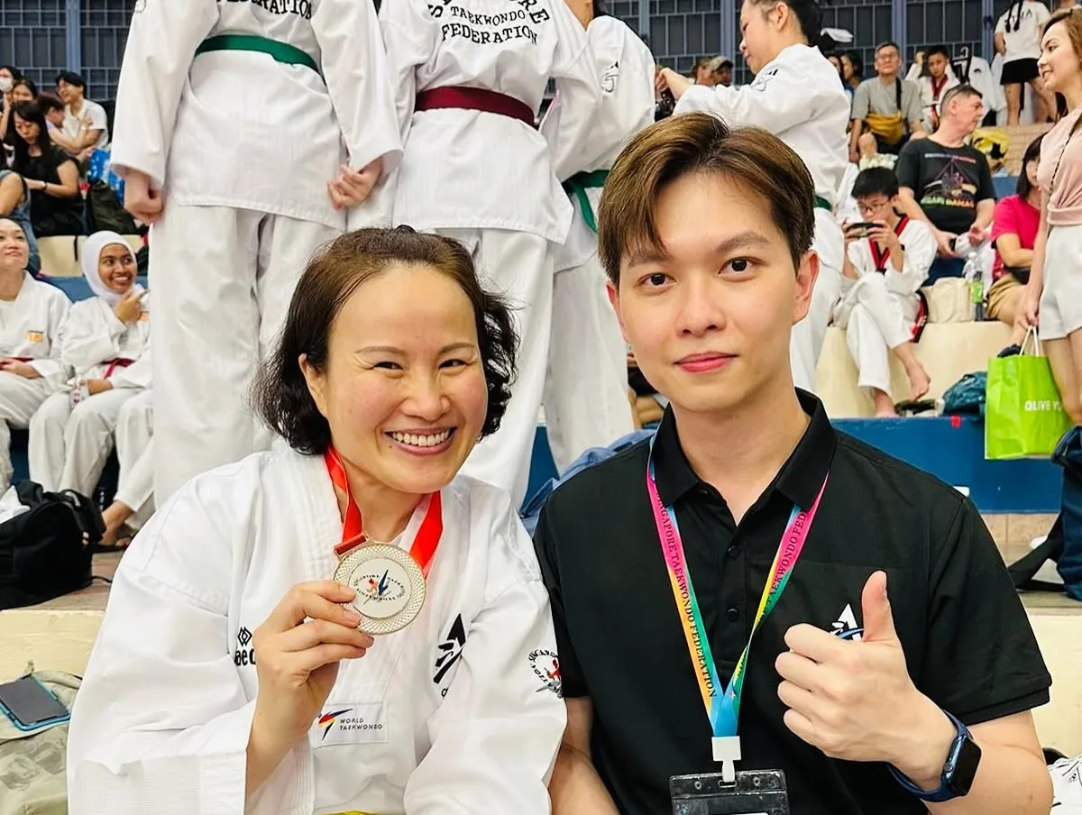 Adult taekwondo student with a competition medal alongside her instructor